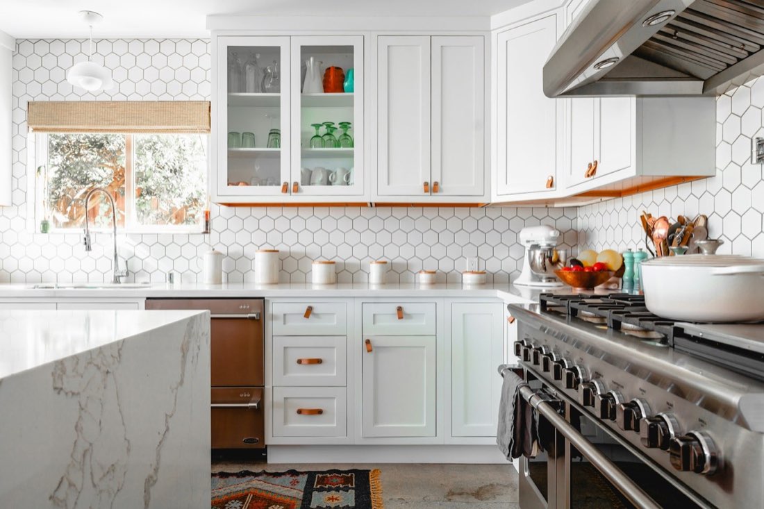 Listing photo of a modern white kitchen with a marble waterfall island and professional range.